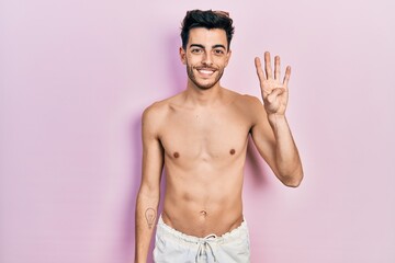 Fototapeta premium Young hispanic man wearing swimwear shirtless showing and pointing up with fingers number four while smiling confident and happy.