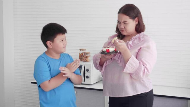 Asian family relationship with son prohibit mother fat eating cake in the kitchen at home, mom eating unhealthy food, two people, woman overweight, mothers day, health care, holiday concept.