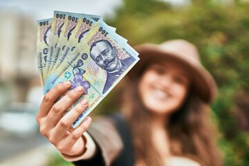 Young hispanic tourist woman smiling happy holding romania lei banknotes at the city.