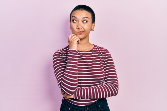 Beautiful hispanic woman with short hair wearing casual striped sweater thinking concentrated about doubt with finger on chin and looking up wondering