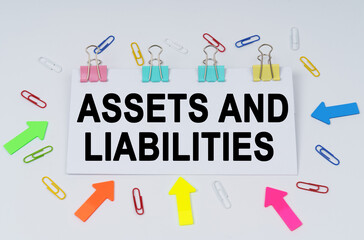 On the table there are paper clips and directional arrows, a sign that says - Assets and Liabilities
