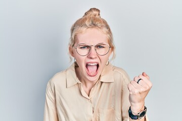 Beautiful caucasian woman with blond hair wearing casual look and glasses angry and mad raising...
