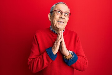Handsome senior man with grey hair wearing casual clothes and glasses begging and praying with...
