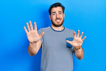 Handsome caucasian man with beard wearing casual striped t shirt afraid and terrified with fear...