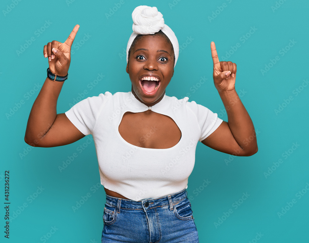 Canvas Prints Young african woman with turban wearing hair turban over isolated background smiling amazed and surprised and pointing up with fingers and raised arms.