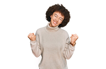 Young hispanic girl wearing wool winter sweater very happy and excited doing winner gesture with arms raised, smiling and screaming for success. celebration concept.