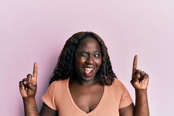 African young woman pointing up with fingers winking looking at the camera with sexy expression,...