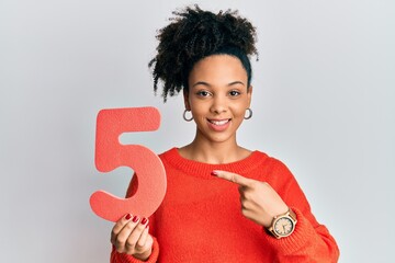 Young african american girl holding number five smiling happy pointing with hand and finger