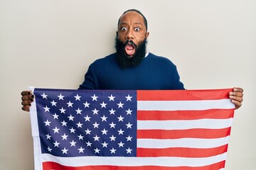 Young african american man holding united states flag afraid and shocked with surprise and amazed expression, fear and excited face.