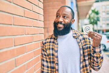 Handsome modern african american man with beard smiling positive standing at the street showing email symbol on paper