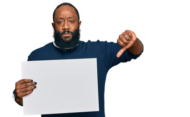 Young african american man holding blank empty banner with angry face, negative sign showing...