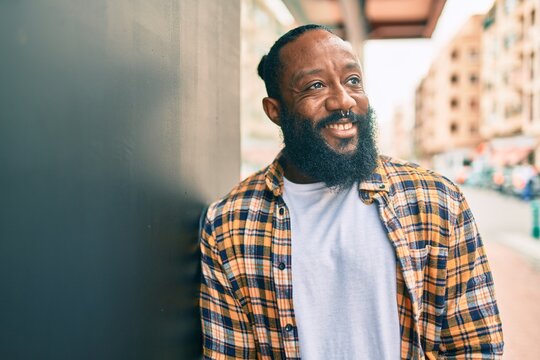 Handsome modern african american man with beard smiling positive leaning over wall