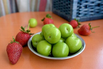 background of green plums in a plate and strawberries on the table