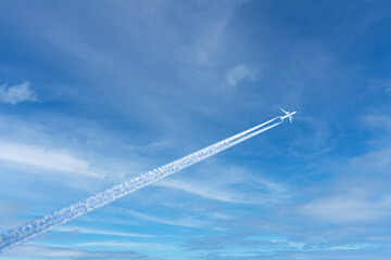 A large airliner flies in the air. There are white clouds and a trail behind the plane in the blue...