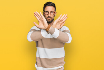 Handsome man with beard wearing casual clothes and glasses rejection expression crossing arms doing negative sign, angry face