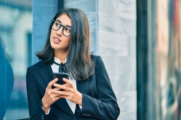 Young hispanic businesswoman smiling happy using smartphone at the city.