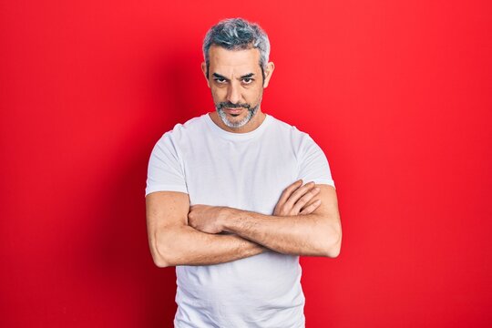 Handsome middle age man with grey hair wearing casual white t shirt skeptic and nervous, disapproving expression on face with crossed arms. negative person.