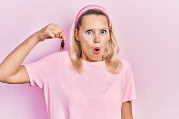Beautiful caucasian blonde woman holding cockroach scared and amazed with open mouth for surprise,...