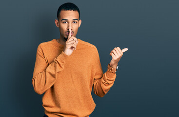 Young african american man wearing casual clothes asking to be quiet with finger on lips pointing with hand to the side. silence and secret concept.