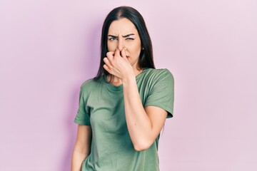Beautiful woman with blue eyes wearing casual t shirt smelling something stinky and disgusting, intolerable smell, holding breath with fingers on nose. bad smell - obrazy, fototapety, plakaty