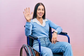 Beautiful woman with blue eyes sitting on wheelchair showing and pointing up with fingers number...