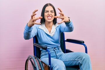 Beautiful woman with blue eyes sitting on wheelchair shouting frustrated with rage, hands trying to strangle, yelling mad