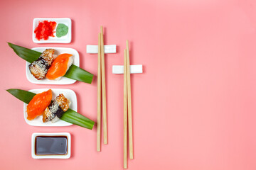 Sushi set with chopsticks and soy sauce on pink minimalistic background.
