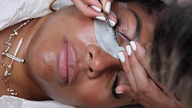 Crop beautician applying eyelashes on face of black woman
