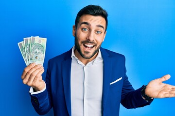 Young hispanic businessman wearing business suit holding polish zloty banknotes celebrating achievement with happy smile and winner expression with raised hand