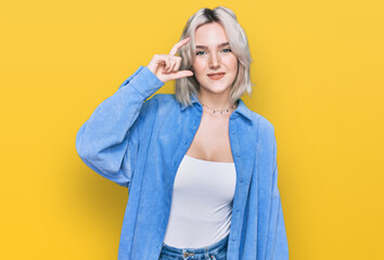 Young blonde girl wearing casual clothes smiling and confident gesturing with hand doing small size sign with fingers looking and the camera. measure concept.