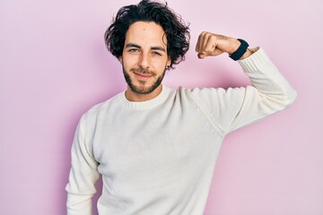 Handsome hispanic man wearing casual white sweater strong person showing arm muscle, confident and proud of power