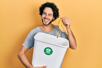 Handsome hispanic man recycling banana peel composting organic fertilizer winking looking at the...