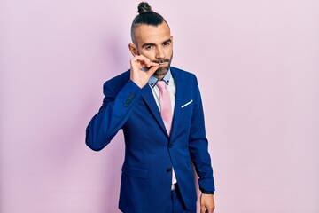 Young hispanic man wearing business suit and tie mouth and lips shut as zip with fingers. secret...