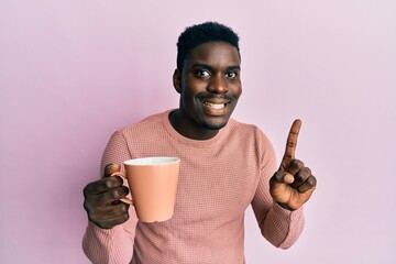 Handsome black man drinking a cup of coffee smiling with an idea or question pointing finger with...