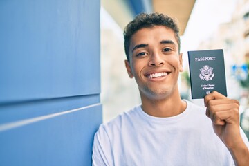 Young latin man smiling happy holding united states passport leaning on the wall at the city.