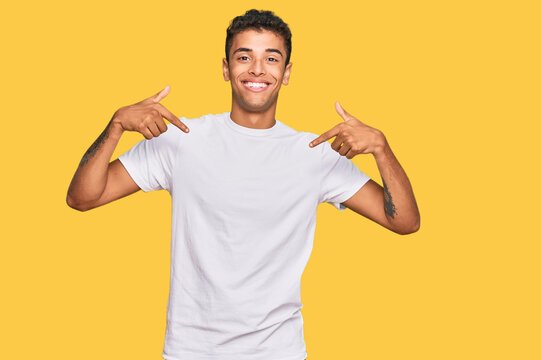 Young handsome african american man wearing casual white tshirt looking confident with smile on face, pointing oneself with fingers proud and happy.