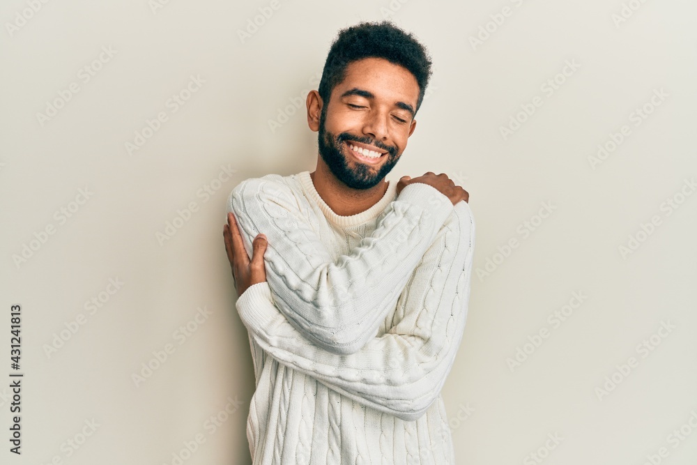 Wall mural Handsome hispanic man with beard wearing casual winter sweater hugging oneself happy and positive, smiling confident. self love and self care