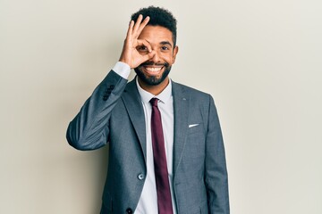 Handsome hispanic man with beard wearing business suit and tie doing ok gesture with hand smiling, eye looking through fingers with happy face.