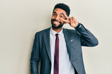 Handsome hispanic man with beard wearing business suit and tie doing peace symbol with fingers over face, smiling cheerful showing victory