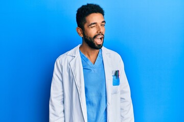 Handsome hispanic man with beard wearing doctor uniform winking looking at the camera with sexy...