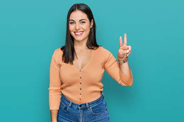 Young hispanic woman wearing casual clothes smiling looking to the camera showing fingers doing victory sign. number two.