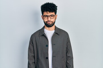 Young arab man with beard wearing glasses puffing cheeks with funny face. mouth inflated with air,...