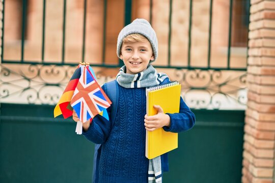 Adorable blond student kid smiling happy holding flags of different countries at the school.