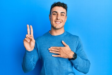 Hispanic young man wearing casual winter sweater smiling swearing with hand on chest and fingers...