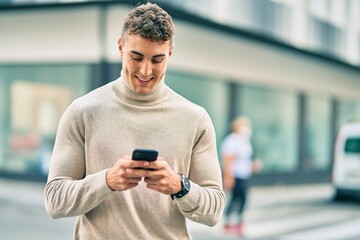 Young hispanic man smiling happy using smartphone at the city.