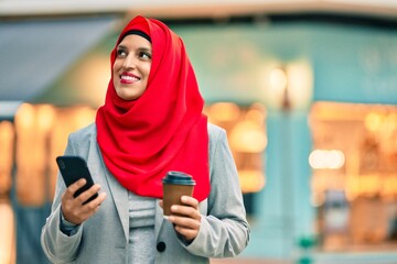 Young arab businesswoman using smartphone and drinking coffee at the city.