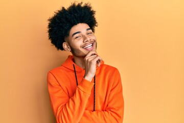 Young african american man with afro hair wearing casual sweatshirt smiling looking confident at the camera with crossed arms and hand on chin. thinking positive.