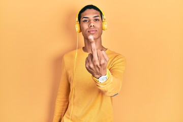Young african american guy listening to music using headphones showing middle finger, impolite and...
