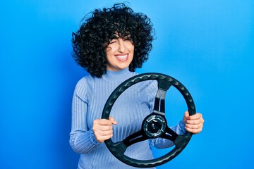 Young middle east woman holding steering wheel winking looking at the camera with sexy expression,...