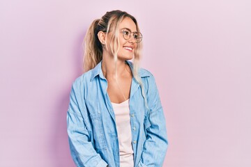 Beautiful young blonde woman wearing casual clothes and glasses looking away to side with smile on...